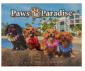 Paws in Paradise 2026 Calendar cover with four dogs wearing leis on a Hawaiian beach