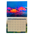 A 2027 wall calendar hanging against a white background, featuring a dramatic volcanic lava flow scene in vivid blue, pink, orange, and red tones. The lower portion shows the September 2027 calendar grid with days of the week and month names in English and Hawaiian.