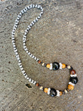 Handmade Hawaiian-style lei necklace with black kukui nuts, light brown wood beads, and white mongo shell accents on a textured stone background