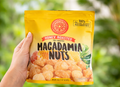 Hand holding a package of honey roasted macadamia nuts with a blurred green background