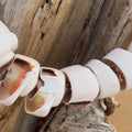 Close-up of necklace with shell beads hanging on a piece of driftwood by a beach.