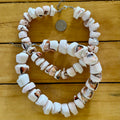 Necklace made of white shell beads on a wooden surface with a coin for scale.