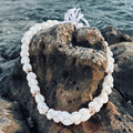 White  bubble shell lei necklace on a textured rock with water in the background