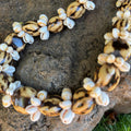 Necklace with white shell rings and marble kukui beads on a dark stone surface
