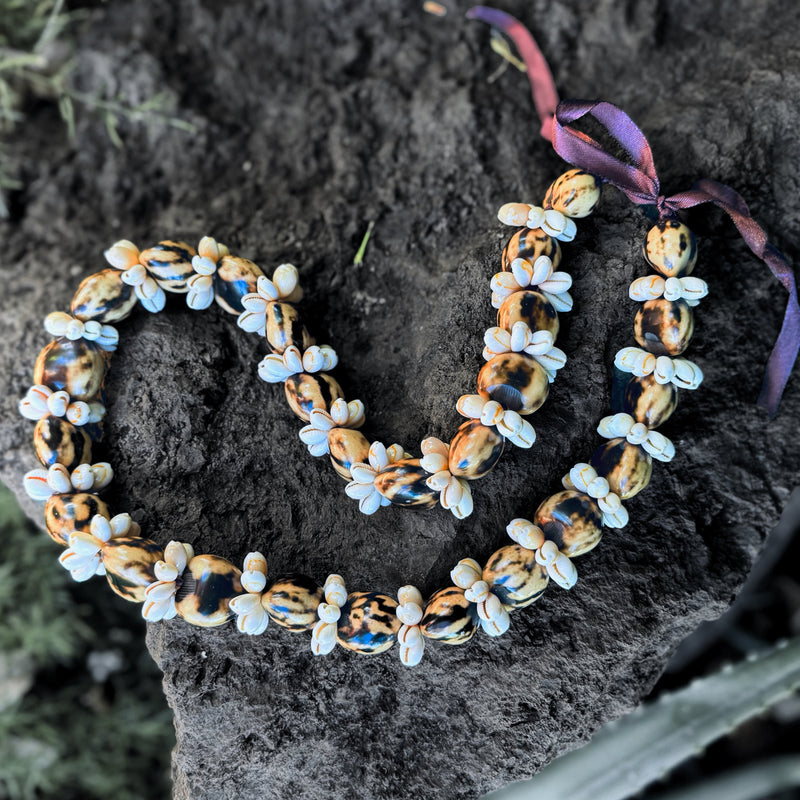 Necklace with white shell rings and marble kukui beads on a dark stone surface