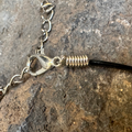 Close-up of a silver clasp on a black cord against a stone background