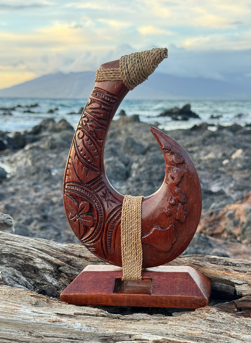 Decorative wooden fish hook with intricate carvings on a rocky beach background