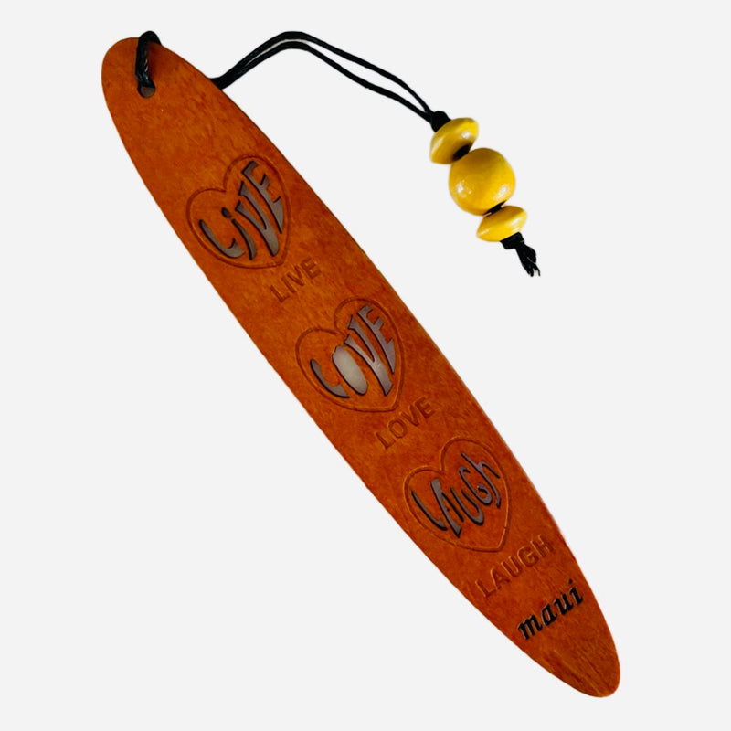 A collection of wooden bookmarks with Hawaiian inspired designs, featuring phrases and images related to Hawaii, displayed on a surface with a floral patterned book in the background.